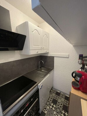A compact kitchen with a microwave, double cabinets, a sink, and a red coffee maker. - Seignosse océan, 2 bedroom apartment, walking distance to the beach, ideal for a family (SEIGNOSSE)