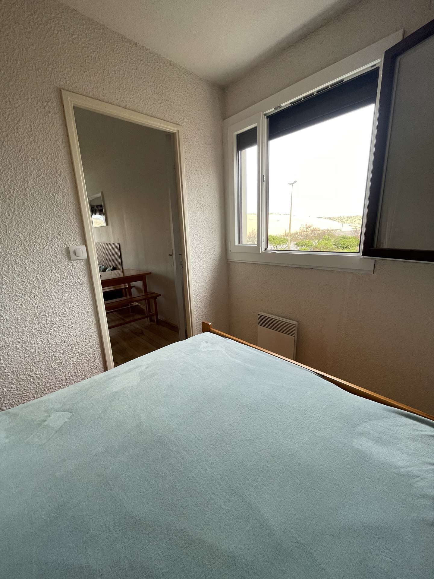 Una camera da letto con un letto, una finestra, un termosifone e una porta che dà su un'altra stanza.