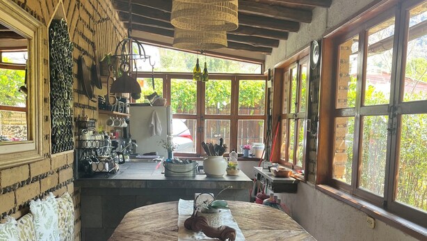 Una cocina rústica con una mesa redonda de madera, una lámpara de mimbre colgante y un perro descansando debajo de la mesa.