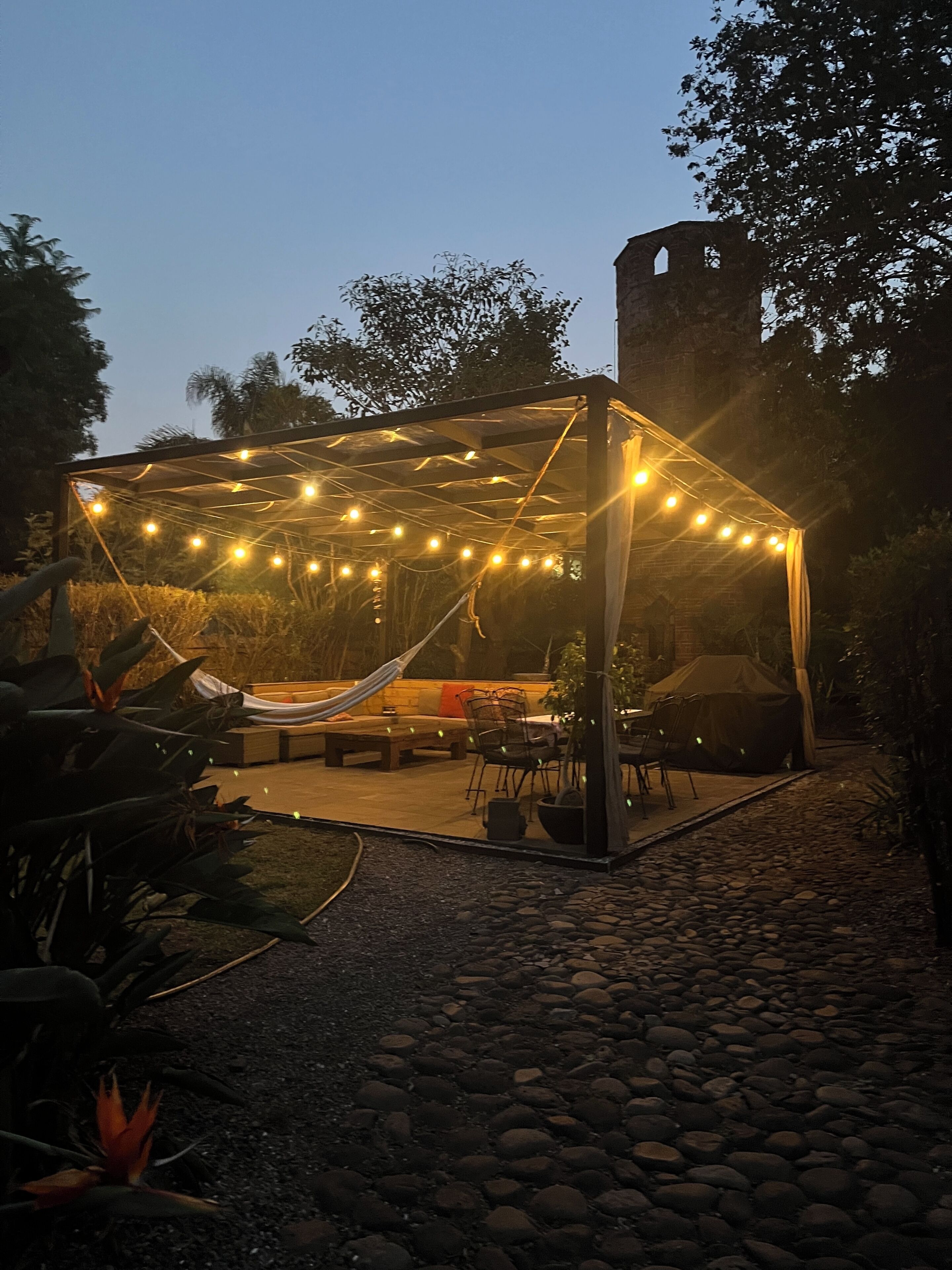 Un espace extérieur aménagé en terrasse, avec des guirlandes lumineuses, un hamac et un coin salon abrité.