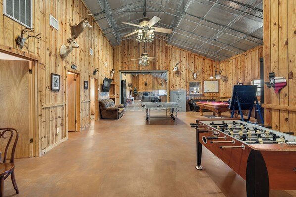 A spacious room with wooden walls, a ceiling fan, a foosball table, and a billiards table.