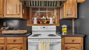 A kitchen with wooden cabinets, a white stove, and a window with decorative items. - Spacious 6-bedroom lodge in beautiful Damon with AC (Damon)