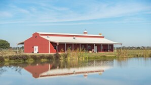 A red barn with a white roof, a door, and windows, situated next to a calm body of water. - Spacious 6-bedroom lodge in beautiful Damon with AC (Damon)