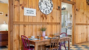 A wooden interior with a wall clock, a welcome sign, a dining table with chairs, and a potted plant. - Spacious 6-bedroom lodge in beautiful Damon with AC (Damon)