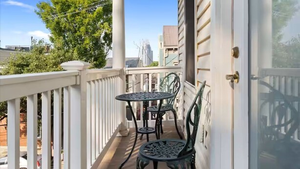 A balcony with a table and chairs, a white railing, and a view of trees and buildings. - Hilltop Haven in Mount Adams (Cincinnati)