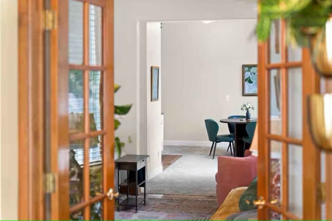An interior view of a room with a wooden door, a dining area with a table and chairs, and a sofa.