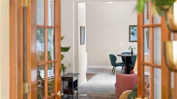 An interior view of a room with a wooden door, a dining area with a table and chairs, and a sofa.