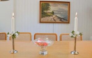 A dining table with two candles, a vase with flowers, and a painting on the wall.