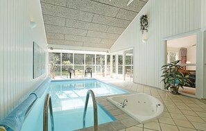 Une piscine intérieure dotée d’un jacuzzi, de grandes fenêtres et d’un plafond à la finition texturée.