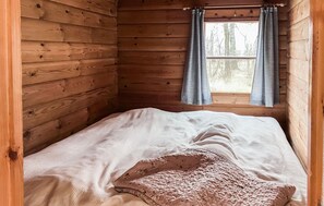 Una habitación de cabaña de madera con una cama individual, una ventana con cortinas y vista a árboles afuera.
