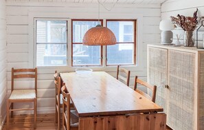 Una mesa de comedor de madera con sillas, una lámpara colgante de fibra natural y un mueble con frente de tejido.