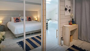 Moderni hotellihuone, jossa on sänky, yöpöytä, peili ja näkymä kylpyhuoneeseen.