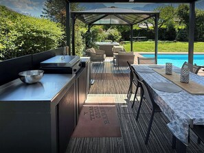 Ein Außenküchenbereich mit Grill, Sitzgelegenheit und Blick auf den Pool.