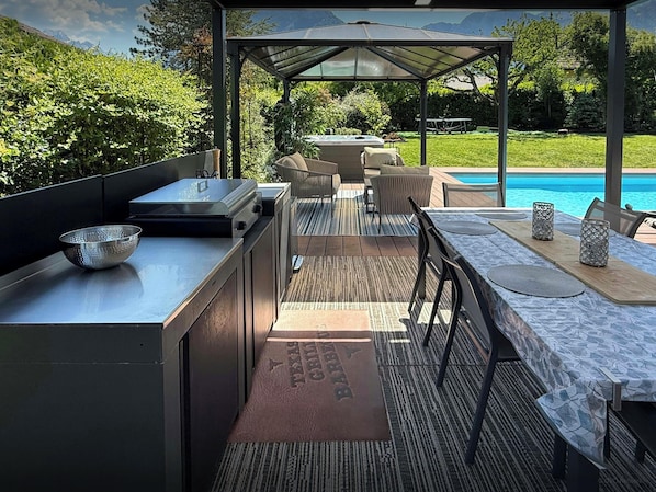 An outdoor kitchen area with a grill, seating, and a pool view.