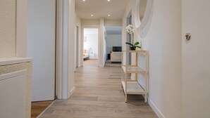 A hallway with a wooden floor, white walls, and a door on the left. - The line Apartment in Zurich Oerlikon (Zurigo)