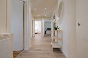 A hallway with a wooden floor, white walls, and a door on the left. - The line Apartment in Zurich Oerlikon (Zurigo)