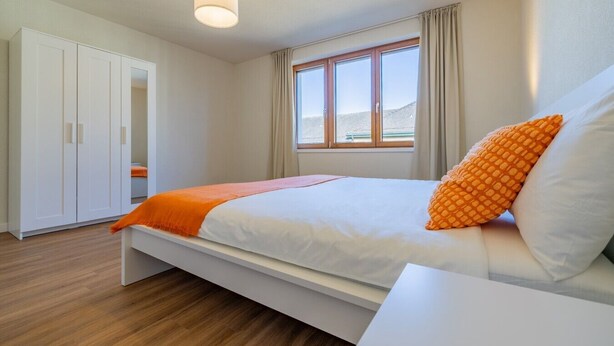 A bedroom with a bed, a wardrobe, a bedside table, and a window. - The line Apartment in Zurich Oerlikon (Zurigo)