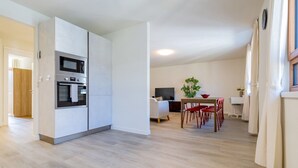 A modern kitchen with built-in appliances, a dining area with a red table and chairs, and a living space with a TV and a plant. - The line Apartment in Zurich Oerlikon (Zurigo)