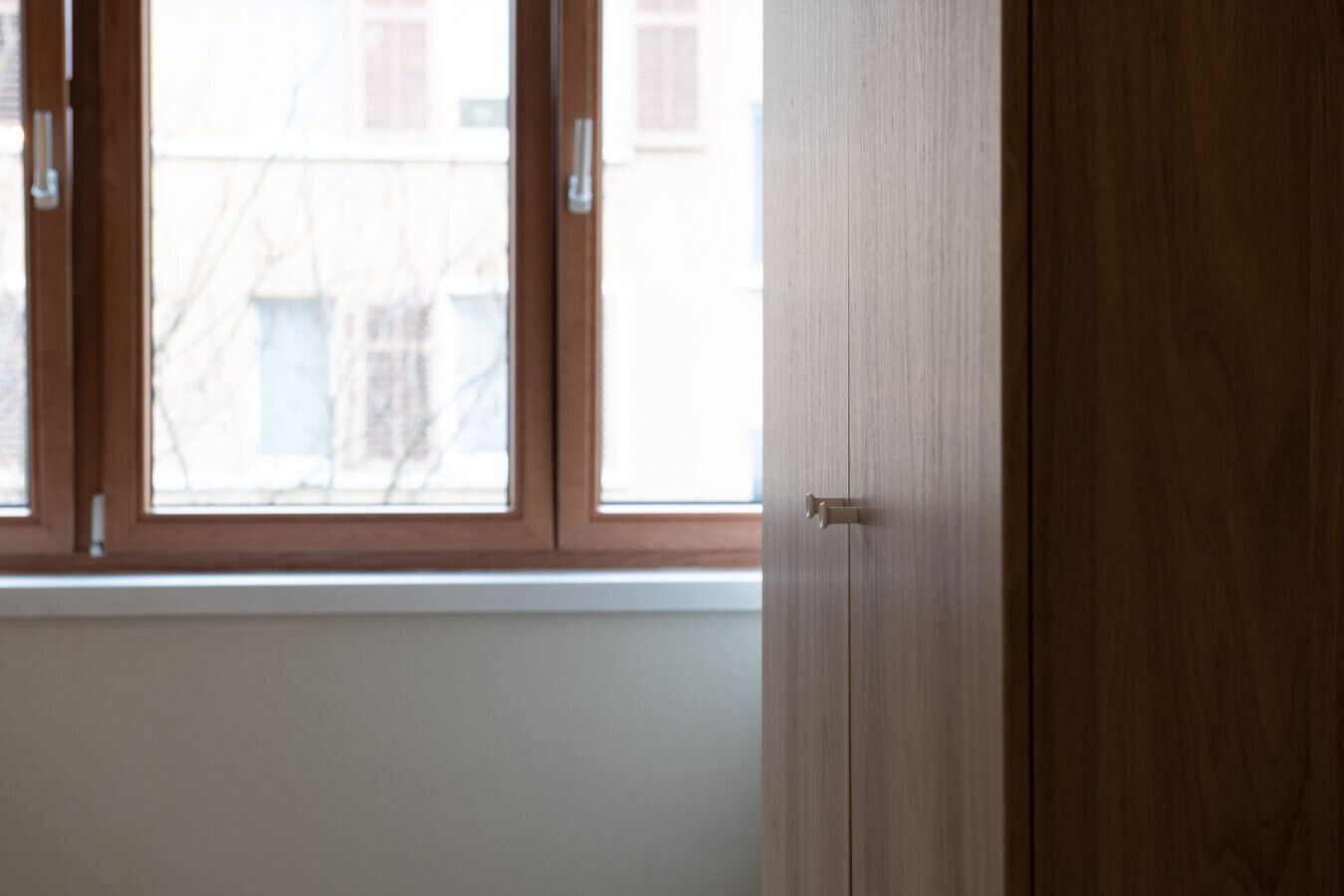 Une pièce avec une porte en bois, une fenêtre avec des stores et une vue sur les bâtiments à l’extérieur.