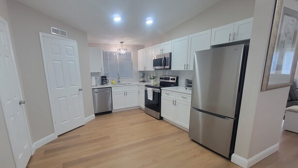 A modern kitchen with white cabinets, stainless steel appliances, and a wooden floor. - Beautiful  Vacation Home in The Villages, Florida – Golf Car Included! (Lady Lake)