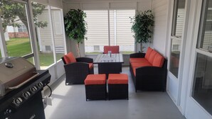 A covered patio with a grill, wicker furniture, and potted plants. - Beautiful  Vacation Home in The Villages, Florida – Golf Car Included! (Lady Lake)