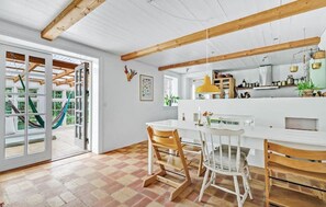A spacious kitchen with wooden beams, a dining area with chairs, and a view of a garden through glass doors. - Cozy home in Kirke Hyllinge with WiFi (Kirke Hyllinge)