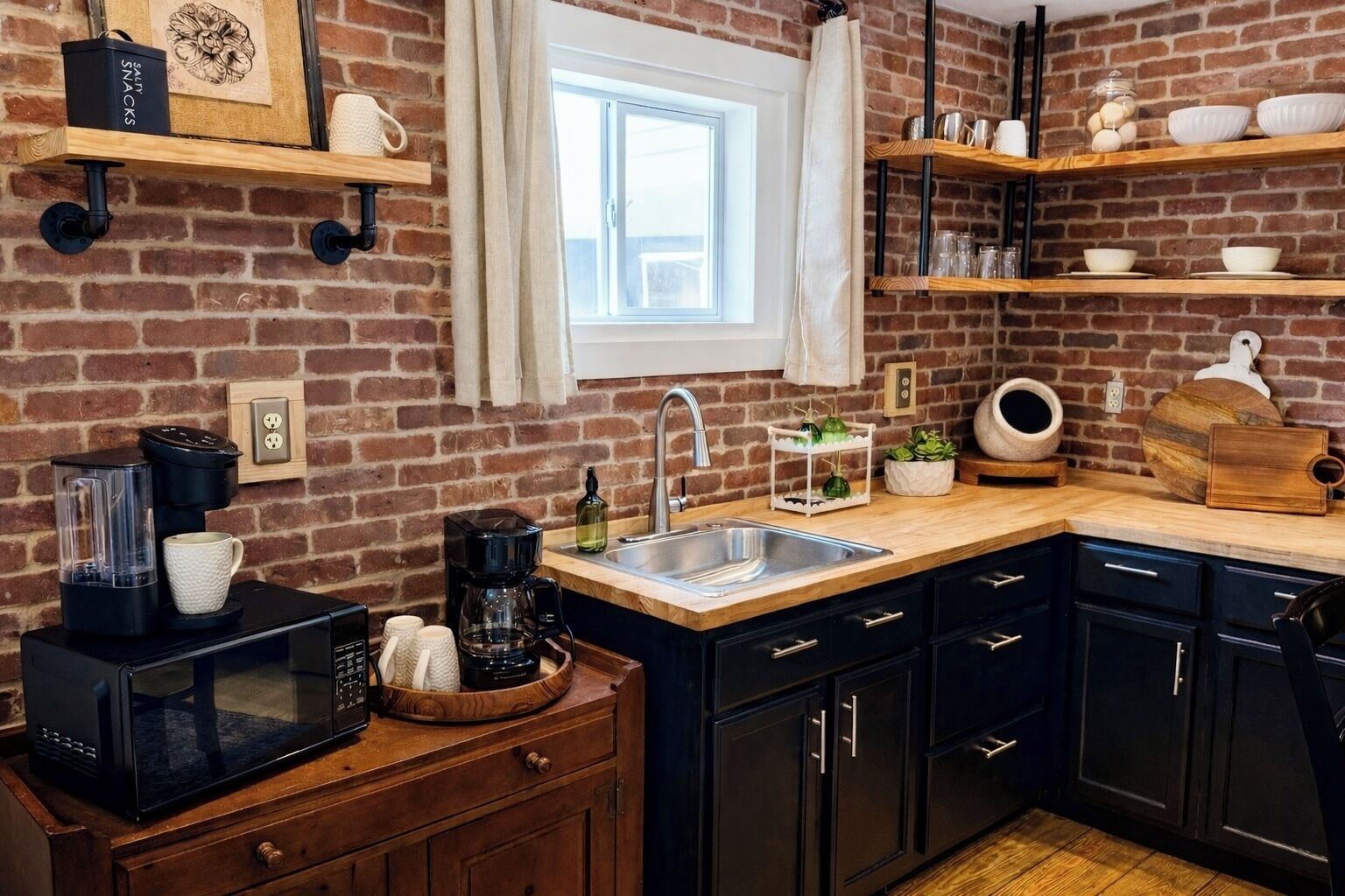 A kitchen with a brick wall, a window, a sink, cabinets, and a countertop with various items.