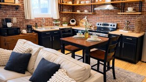 Une cuisine moderne avec des murs en briques, des étagères en bois, une table à manger avec des chaises et un canapé avec des coussins.