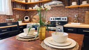 Une cuisine moderne avec des murs en briques, des étagères en bois et une table à manger agrémentée de bols blancs et d’un vase de fleurs.
