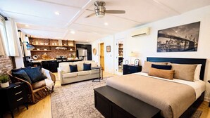 Une chambre moderne avec un grand lit, un bureau et, au fond, un coin cuisine.