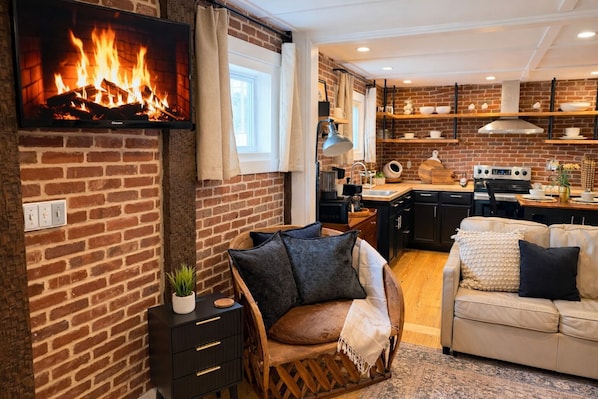 A cozy living area with a fireplace, a sofa, a dining table, and a kitchen with brick walls.