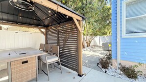 En uteplats med ett bord och stolar, en pergola och ett hus i bakgrunden.