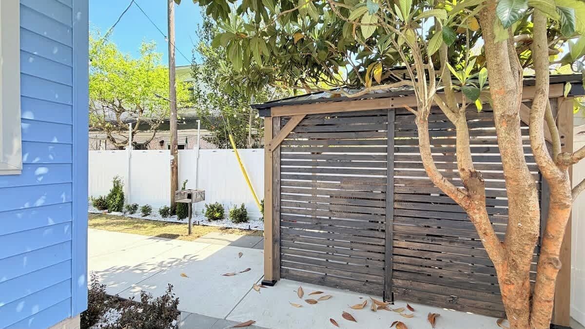 Una casa azul con puerta de garaje de madera, un árbol y una valla blanca al fondo.