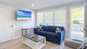 Un salon avec un canapé bleu, une table basse, un téléviseur fixé au mur et de grandes fenêtres.