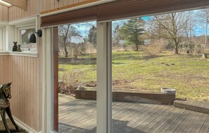 Una habitación con un amplio ventanal corredizo que da a una terraza exterior con vistas a un campo y árboles.