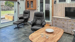 A modern living room with a large TV, leather chairs, a wooden coffee table, and a cabinet with drawers. - 2 bedroom awesome home in Stenlille (Stenlille)
