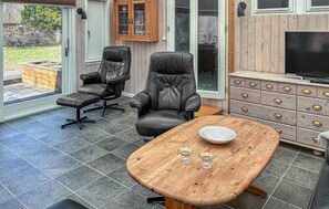 A modern living room with a large TV, leather chairs, a wooden coffee table, and a cabinet with drawers.
