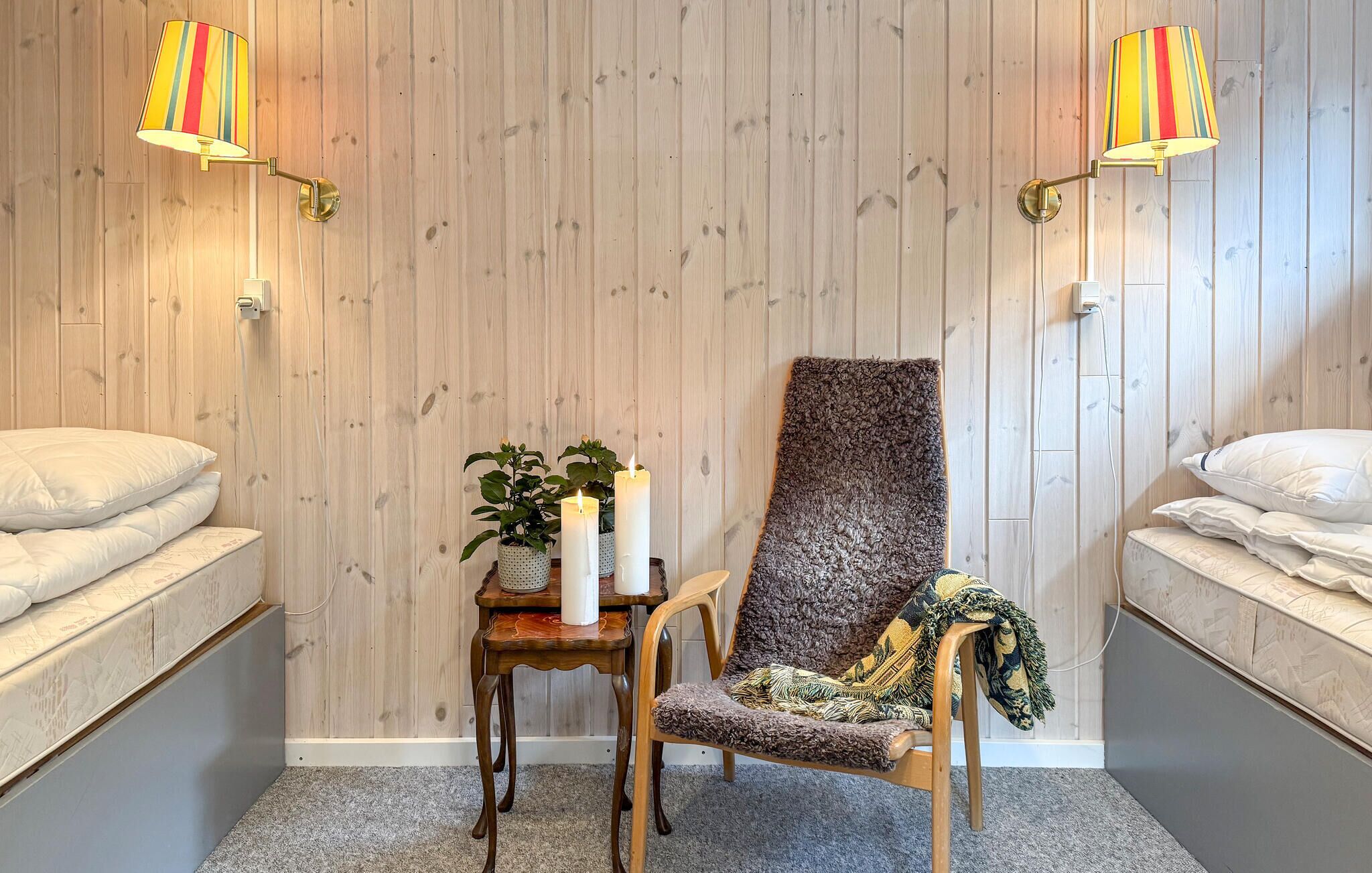 Een kamer met twee bedden, een stoel, een tafel met een plant en kaarsen, en twee wandlampen.