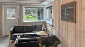 A room with a black leather sofa, a round wooden table, a vase with branches, and a painting on the wall. - 2 bedroom awesome home in Stenlille (Stenlille)