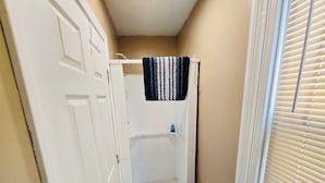 A small, enclosed shower area with a white door, a towel rack, and a toilet paper holder.