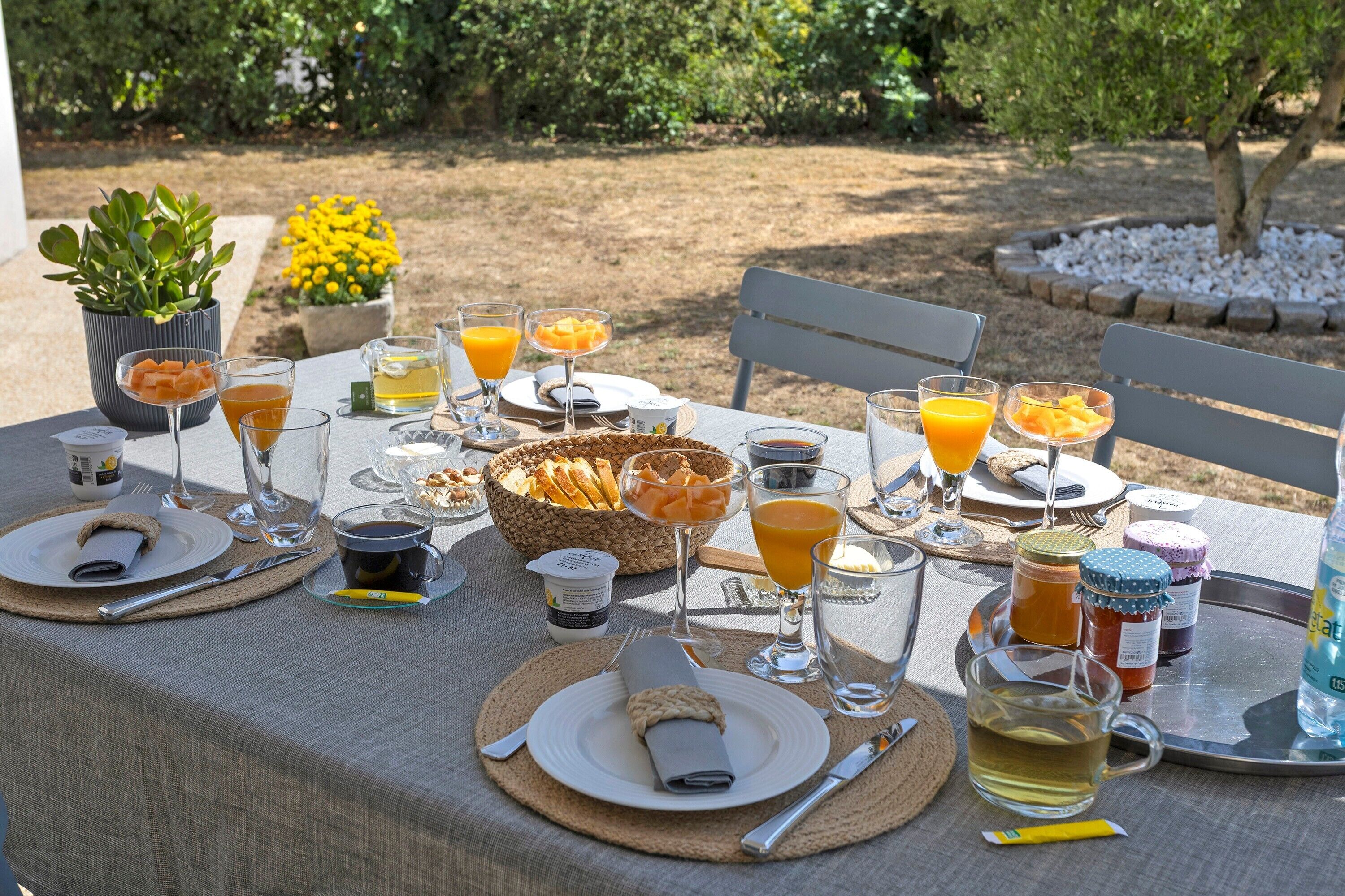 Mesa de comedor al aire libre dispuesta con artículos de desayuno, incluyendo frutas, bebidas y salsas.