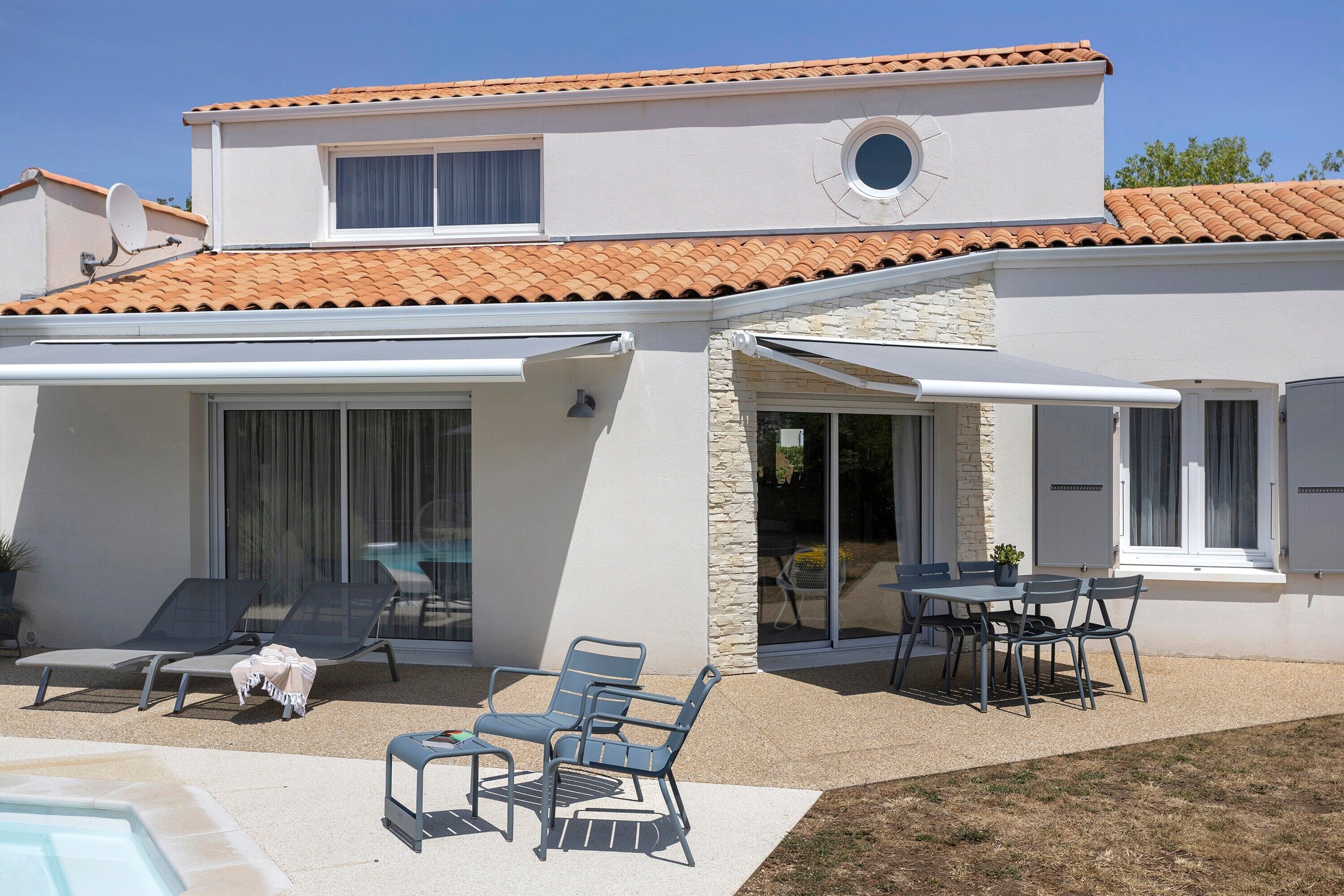 A two-story building with a covered patio area featuring outdoor furniture and a swimming pool.