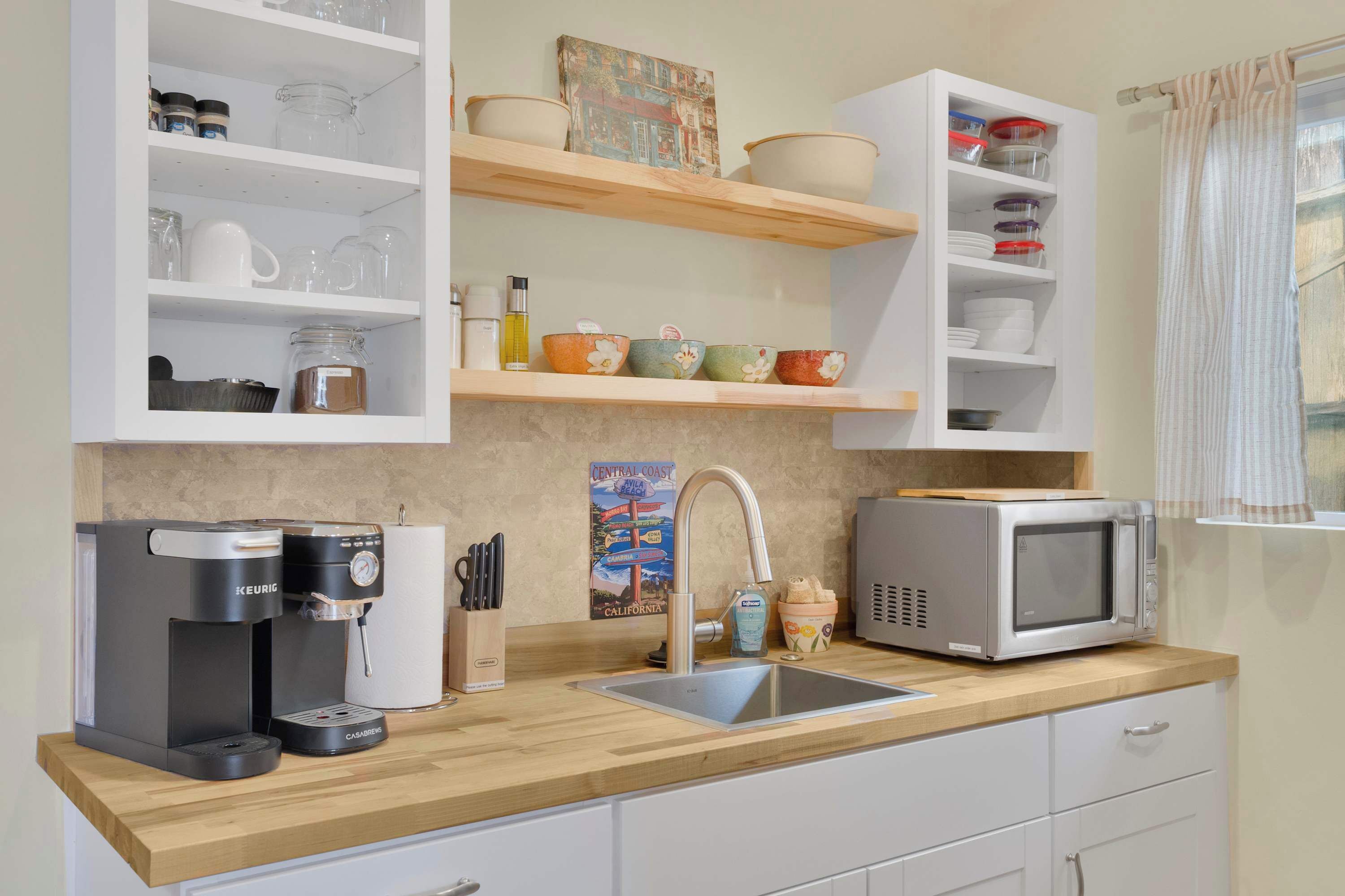 A kitchen with a coffee maker, microwave, sink, and shelves with dishes and jars.