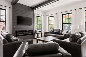 A modern living room with leather sofas, a flat-screen TV, and large windows.