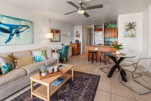 A living room with a sofa, coffee table, and a dining area with a glass table and chairs. - Kihei Maui Vista Condo | 3 Pools, Walk to Beach, Tennis, Pickleball, AC (Kihei)