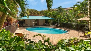 A swimming pool with a sunshade, surrounded by palm trees and a fenced patio area. - Kihei Maui Vista Condo | 3 Pools, Walk to Beach, Tennis, Pickleball, AC (Kihei)