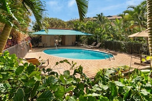 A swimming pool with a sunshade, surrounded by palm trees and a fenced patio area. - Kihei Maui Vista Condo | 3 Pools, Walk to Beach, Tennis, Pickleball, AC (Kihei)