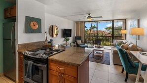 A modern kitchen with a central island, a dining area with a sofa and table, and a balcony with a view. - Kihei Maui Vista Condo | 3 Pools, Walk to Beach, Tennis, Pickleball, AC (Kihei)