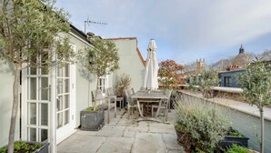 A courtyard with a table and chairs, potted plants, and a white statue. - Divine Mews House - South Kensington (London)