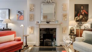 A living room with a fireplace, red and white sofas, a glass coffee table, and various wall art. - Divine Mews House - South Kensington (London)